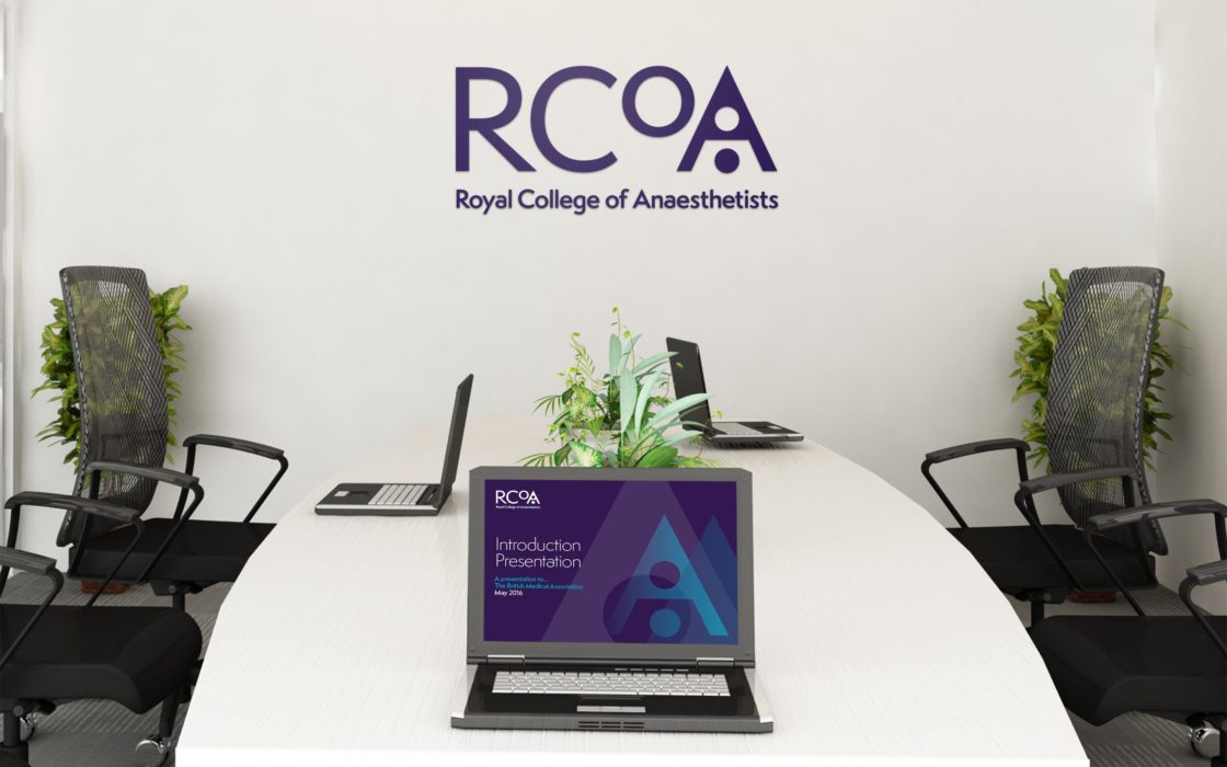Meeting room with RCoA logo on the back wall and a laptop displaying branding presentation.