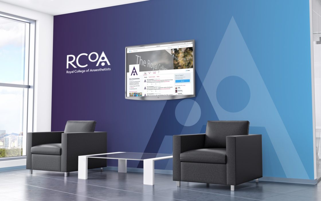 Waiting area with arm chairs and coffee table infant of a two tone wall (purple and blue) with the RCoA logo and TV displaying the Twitter page.