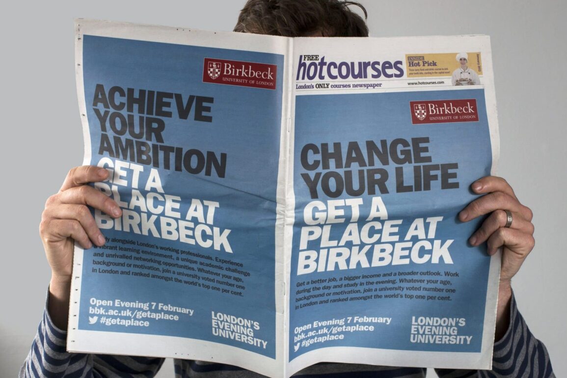 Man holding up a open an open newspaper infant of his face.