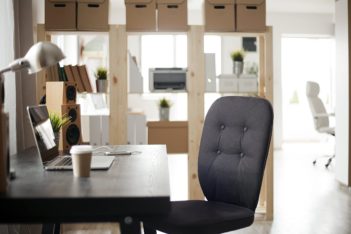 Photo of a home office with desk which has a laptop, speakers, phone and coffee in foreground.
